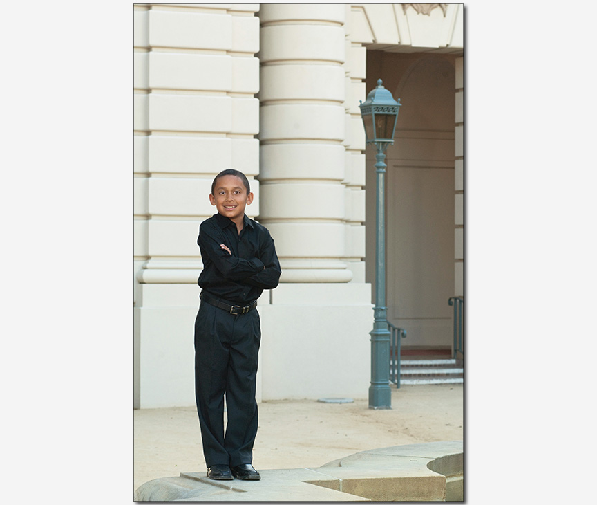 boy posed on fountain with retro building in background